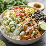 A bowl of food with rice, beans, corn, tomatoes, lime, and avocado.