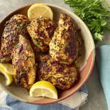 A bowl of marinated chicken with lemon wedges.