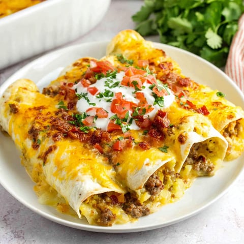 A plate of breakfast enchiladas with tomatoes and cheese.
