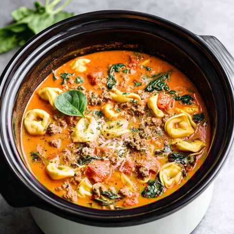 A crockpot filled with tortellini soup and sausage.